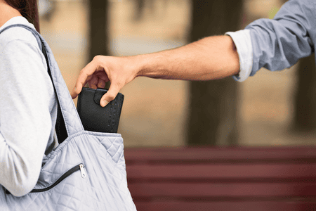 A pickpocket stealing a wallet from a woman's bag